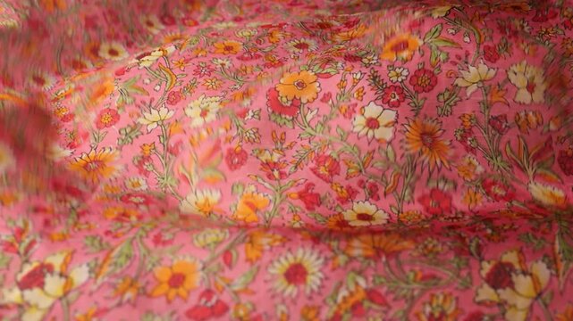 Natural silk fabric with a vintage floral pattern waves in the wind. Flowing pink material creates abstract waves for a motion background. Summer garden print on authentic natural silk textile ripples