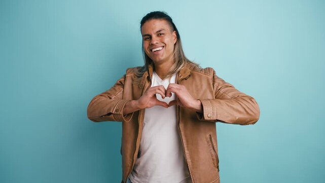 Handsome man with long hair blowing kisses to the camera. He is gesturing with his hands to form a heart, expressing love and affection
