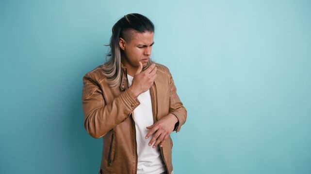 Latin man with long hair pinching his nose from a terrible odor. Unpleasant smell making him feel sick and disgusted against a blue background