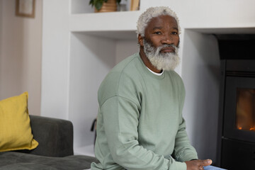 Naklejka premium Senior African American man sitting on gray sofa at home, wearing sage top, watching stove flame