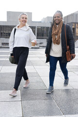 Senior diverse female friends walking across plaza outside civic building, holding coffee cups © wavebreak3