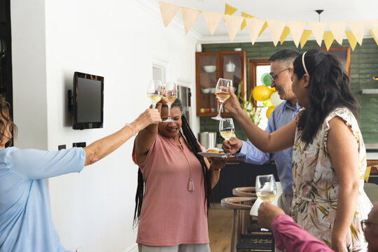 Multi-generational family and friends toasting in home kitchen, holding wine glasses and appetizers