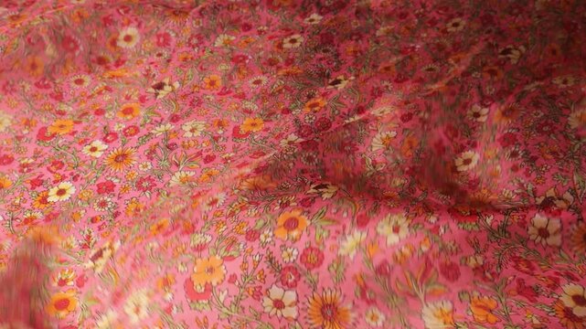 Red and pink natural silk fabric with small floral pattern blowing in the wind. Flowing movements of high quality textile create an abstract background with soft waves. Colorful botanical print.