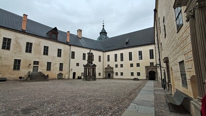 Inner courtyard of Kalmar Castle featuring historic stone architecture, a central well structure and cobblestone ground under an overcast sky. © Pim