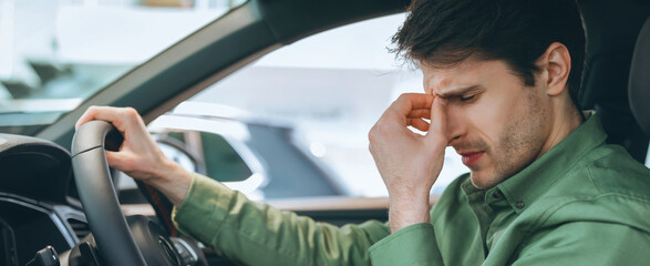 Naklejka premium A man is in a car with a worried expression on his face. He is sitting in the driver's seat and seems to be dealing with stress or anxiety. It is daytime outside.