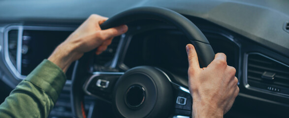 Naklejka premium A person grips the steering wheel of a modern car while driving. Hands are positioned firmly on the wheel for control. The scene is set in a vehicle during daylight.