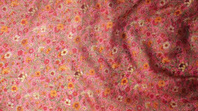 Flowing natural silk fabric with small floral pattern waving in the wind. Abstract background of soft waves and ripples in pink and orange tones. 