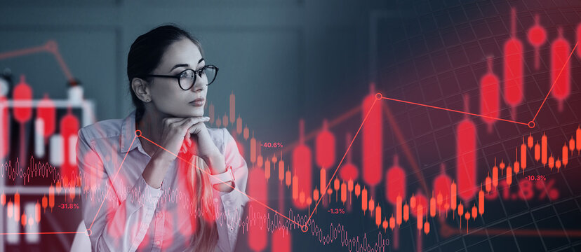 A businesswoman looks thoughtfully at financial data displayed on a screen. It is late at night and she appears focused. The scene shows graphs and charts in red tones.