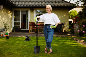 Woman with shovel standing on lawn in backyard garden