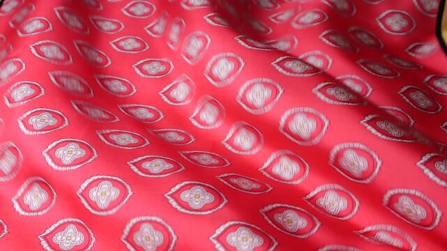 Natural silk fabric with red ethnic paisley pattern blowing in the wind. Abstract background of moving soft waves and smooth textile texture. Elegant red and silver silk material rippling.