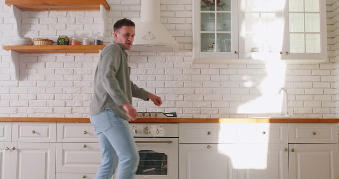 Happy man dancing in kitchen to pretend to be rock musician playing guitar on stage, funny performance rockstar at concert. Cheerful dance of dancer enjoying music rhythm, carefree movements at home