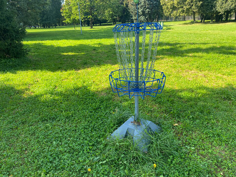Professional disc golf target standing in sunny public park. Metal chain holder and basket mounted on silver pole for outdoor recreation and sporting activities