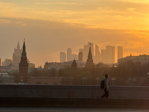 Moscow city skyline with Kremlin towers and skyscrapers at golden sunset. Kremlin wall towers and Moscow City business district skyscrapers under orange evening sky. Urban landscape in golden hour