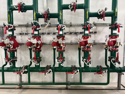 Industrial fire sprinkler system control valves and piping manifold. Complex fire protection water supply system featuring alarm check valves, pressure gauges, and steel pipes.