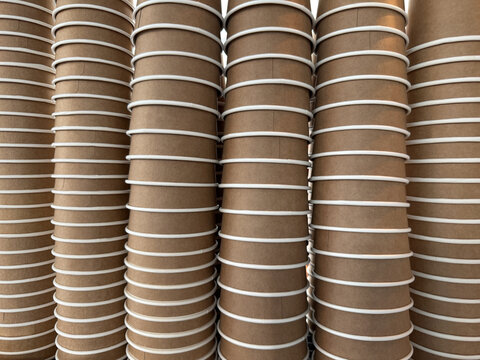 Row of stacked cardboard cups for hot beverages. Disposable eco friendly containers for takeaway coffee and tea. Recyclable paper drinkware arranged on counter in coffee shop.