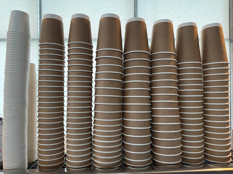 Stacks of disposable brown and white paper coffee cups in cafe. Disposable eco friendly containers for takeaway coffee and tea.