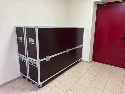 Heavy duty road cases for touring equipment storage. Black plywood trunks with aluminum edges and casters positioned near red door in building corridor.
