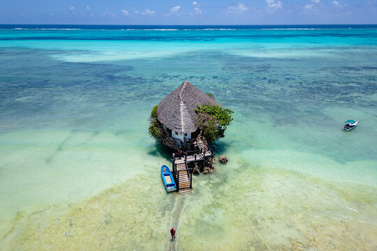 Aerial view of the building surrounded by turquoise water and white sand beach with boats under a clear blue sky in Zanzibar.