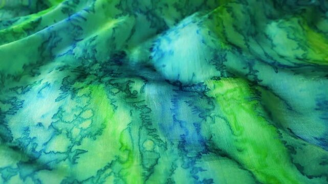 Natural silk fabric with green and blue abstract patterns blowing in the wind. Soft waves of textile creating a fluid motion background. Rippled surface of silk material.
