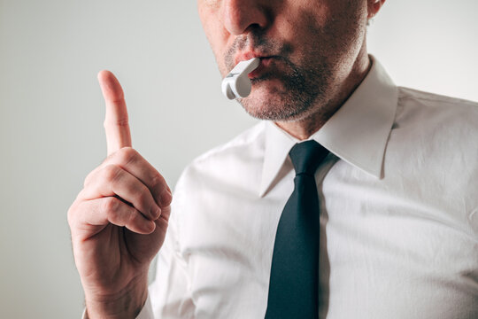 Businessman blowing whistle with raised finger warning gesture, concept of whistleblower