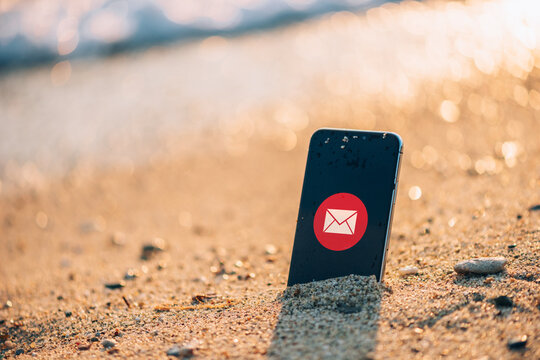 Smartphone with message notification icon stuck in wet sand on a beach at sunset, symbolizing digital communication and vacation