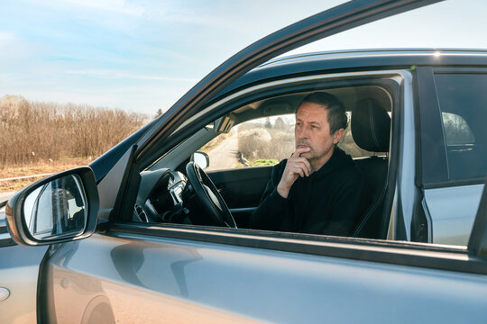Nervous middle-aged man waiting for road assistance after vehicle breakdown in driver&rsquo;s seat, glancing out window in anxious idle moment inside car