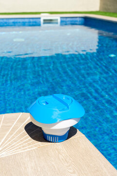 Plastic floating chlorine dispenser resting on pool edge with clear blue water in background - pool maintenance concept