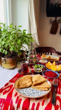 Traditional breakfast with blini pancakes, red caviar, sour cream, and Turkish tea on a table with Ikat pattern runner. Healthy snacks with oranges, lime, and pumpkin seeds in a cozy home setting.