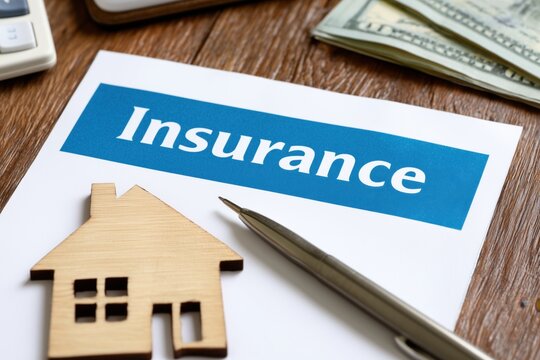 the image captures a flat lay of items on a wooden table, emphasizing home insurance a prominent white document features a blue band with the word "insurance" in white capital letters Generative AI
