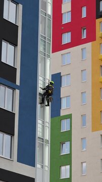 Industrial mountaineering man worker applying washing foam on glazing using microfiber sponge. Male rope access laborer in work uniform during high-rise job. Industry urban works concept.