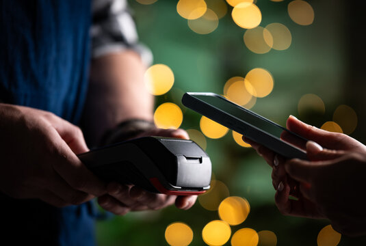 Waiter Holds A Pos Payment Terminal As A Girl Pays For The Bill Against A Blurred Christmas Background