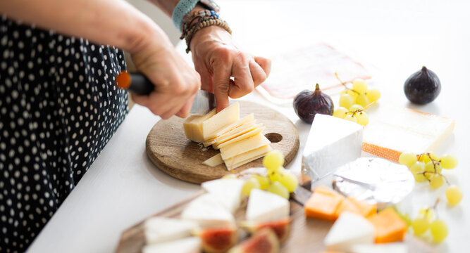 Woman Cutting Parmesan Cheese On A Cutting Board With A Knife
