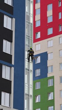Industrial mountaineering man worker applying washing foam on glazing using microfiber sponge. Male rope access laborer in work uniform during high-rise job. Industry urban works concept.