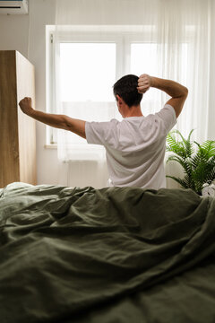Man Stretches and Wakes up in Bedroom During Morning in a Bright and Cozy Room With Plants