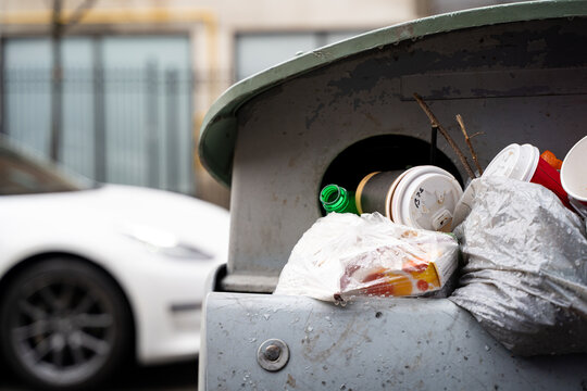 Close up of garbage bags and disposable cups in overflowing trash bin.