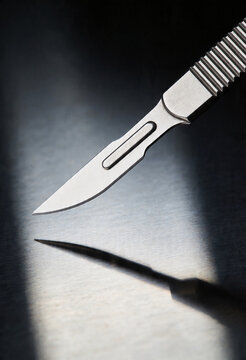 A sharp surgical scalpel blade making a precise incision on skin in a black and white image