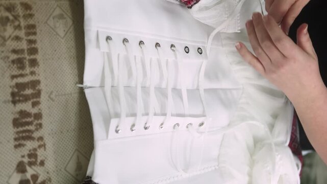 Garment making. Adjustable clothing. Female tailor hands lacing white textile elegant corset dress. Stylish industry professional work.