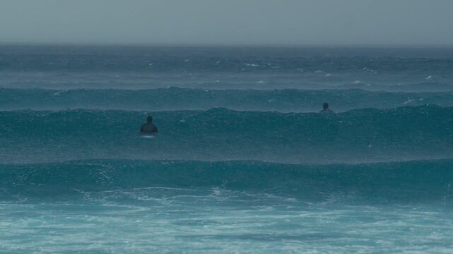 Group of Surfers Sits In Stormy Ocean, Facing Distant Boat Through Heavy Rain And Mist Moody Teal Tones, Overcast Sky, Soft Swells, Contemplative Pause And Quiet Isolation