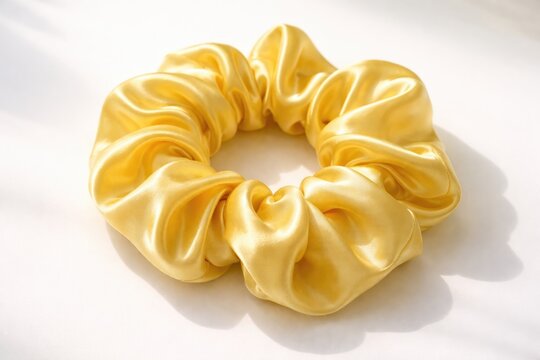 Silky yellow scrunchie hair accessory in satin fabric on white surface