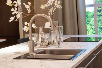 Modern luxury kitchen island with marble countertop, stainless steel sink, and elegant faucet.Minimalist kitchen interior design featuring a marble island and decorative spring blossoms. © Anna Kondratiuk