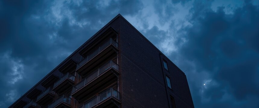 multilevel building facade with balconies facing a twilight cloudy sky