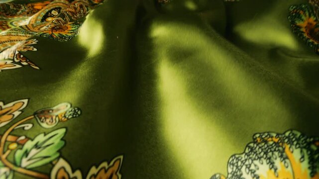 Green silk fabric with floral pattern waving in the wind. Abstract background of moving soft waves. Realistic silk texture with elegant ornaments in olive and orange colors. 