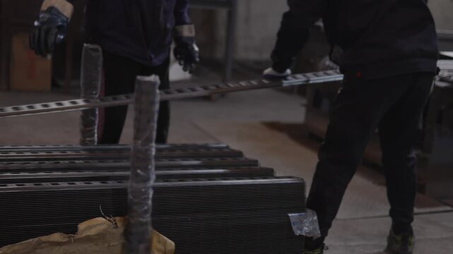 Industrial worker engaging in the manual handling and adjusting of heavy metal bars on a manufacturing line, showcasing labor and production in dimly lit factory environment