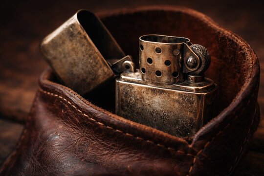 Macro view of an antique style lighter resting in an aged leather pouch with open top