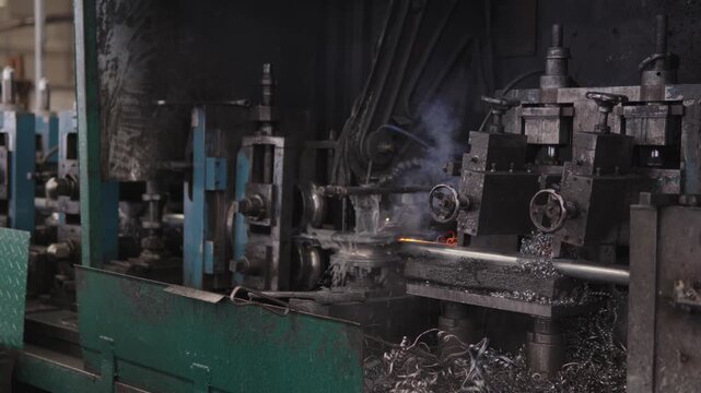 Manufacturing process producing steel pipes, showing metal grinding and sparks flying from the machinery in continuous industrial production line within a metalworking factory