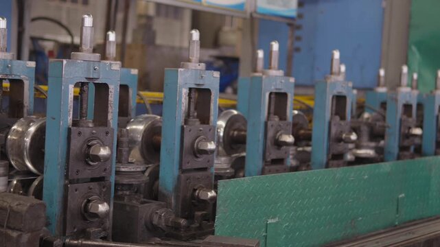 Industrial manufacturing equipment working on production line in large scale factory, fabricating metal products with numerous rollers and guiding mechanisms