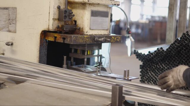 Worker operating punching machine to bore holes in aluminum profiles on a factory production line, showing metalworking precision, safety gear and industrial equipment