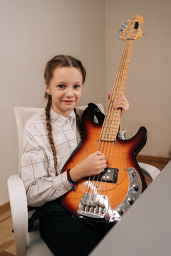 Vertical portrait of pretty cute child girl with pigtails holding bass guitar and smiling, practicing musical notes and developing a new skill, finding joy and expression in instrumental learning.