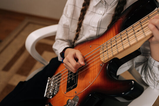 Close-up cropped shot of preteen girl holding electric bass guitar and smiling, happily learning creating music, enjoying her musical hobby and development.