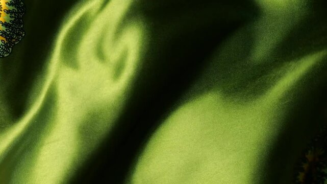 Natural silk fabric with floral pattern fluttering in the wind. Green textile material creates abstract waves background. Detailed view of flowing smooth cloth with yellow flowers ornament.